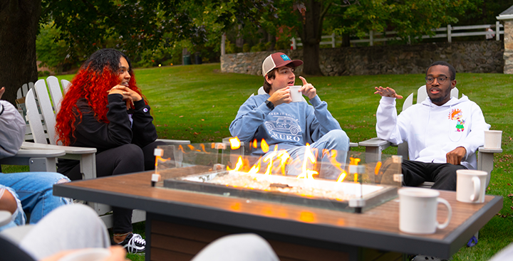 鶹Ƶ Student Admission tour guides converse and have hot cocoa at the firepit on campus.
